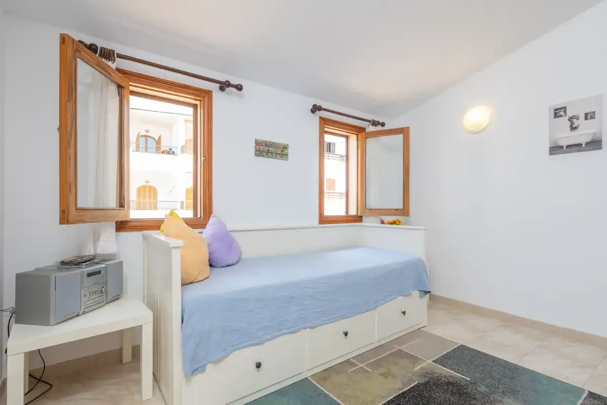A bright bedroom with a single bed beneath two open wooden windows.