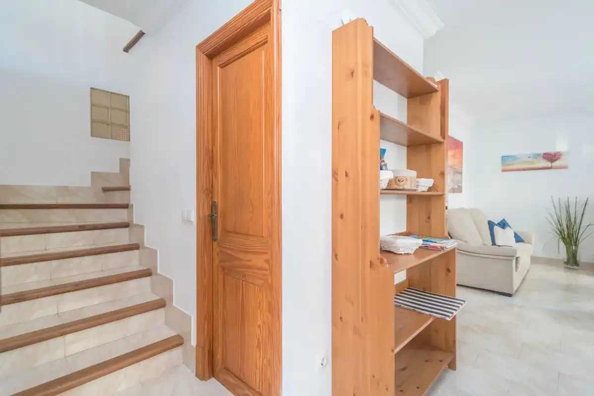 A bright living area with a staircase, wooden shelving, and seating.