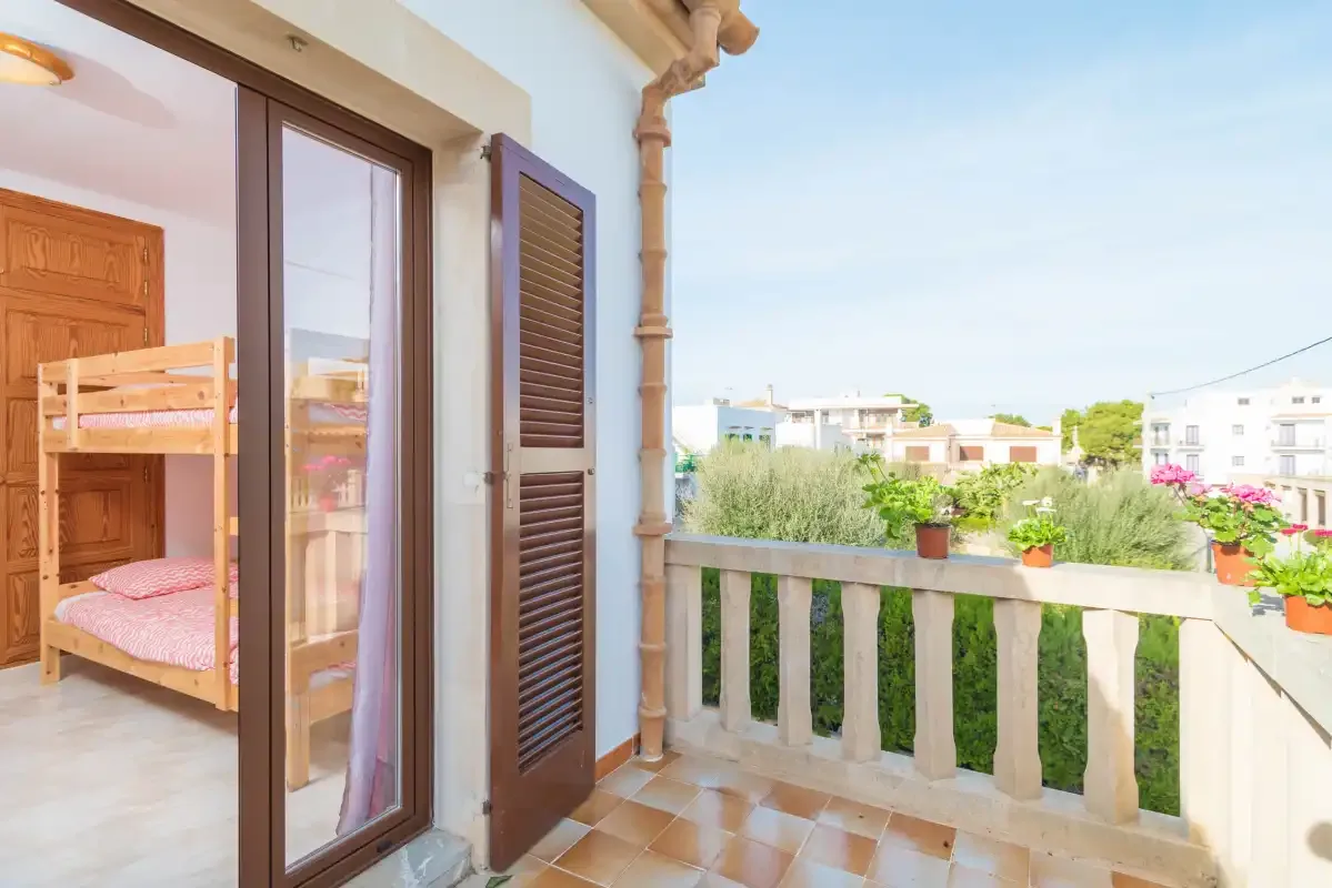 A balcony overlooks nearby buildings and greenery, with a bunk bed visible indoors.