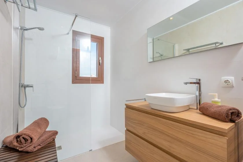 A bright bathroom with a shower, a wooden vanity, and a small window.