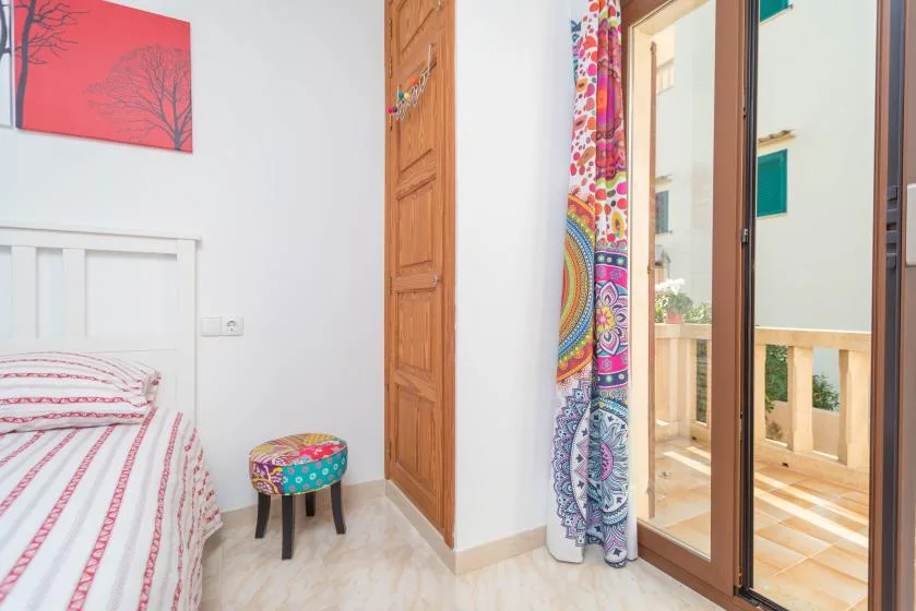 A bedroom with a single bed, a wooden door, and colorful curtains beside a glass door.