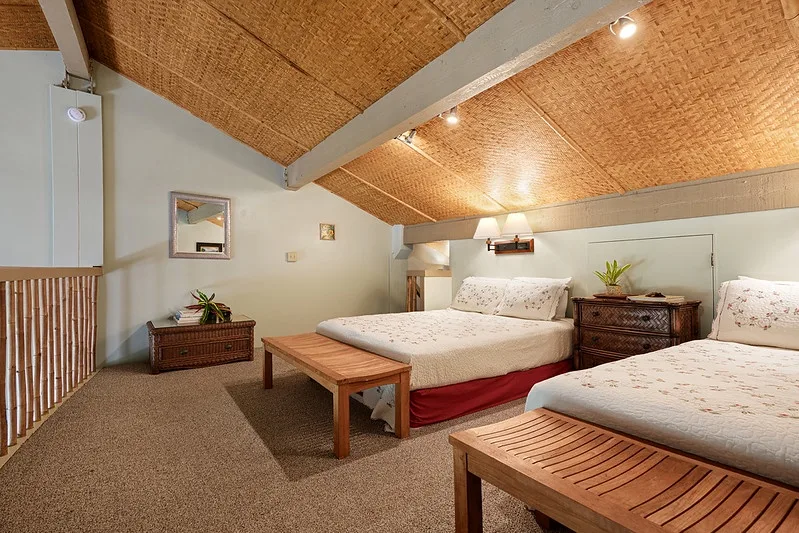 A bedroom with two beds, wooden furnishings, and a sloped woven ceiling.