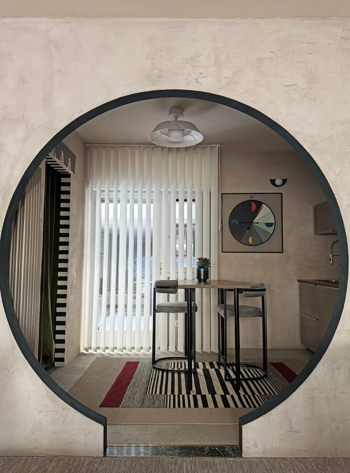 Comedor con una mesa alta y persianas verticales, visto a través de un arco redondo.