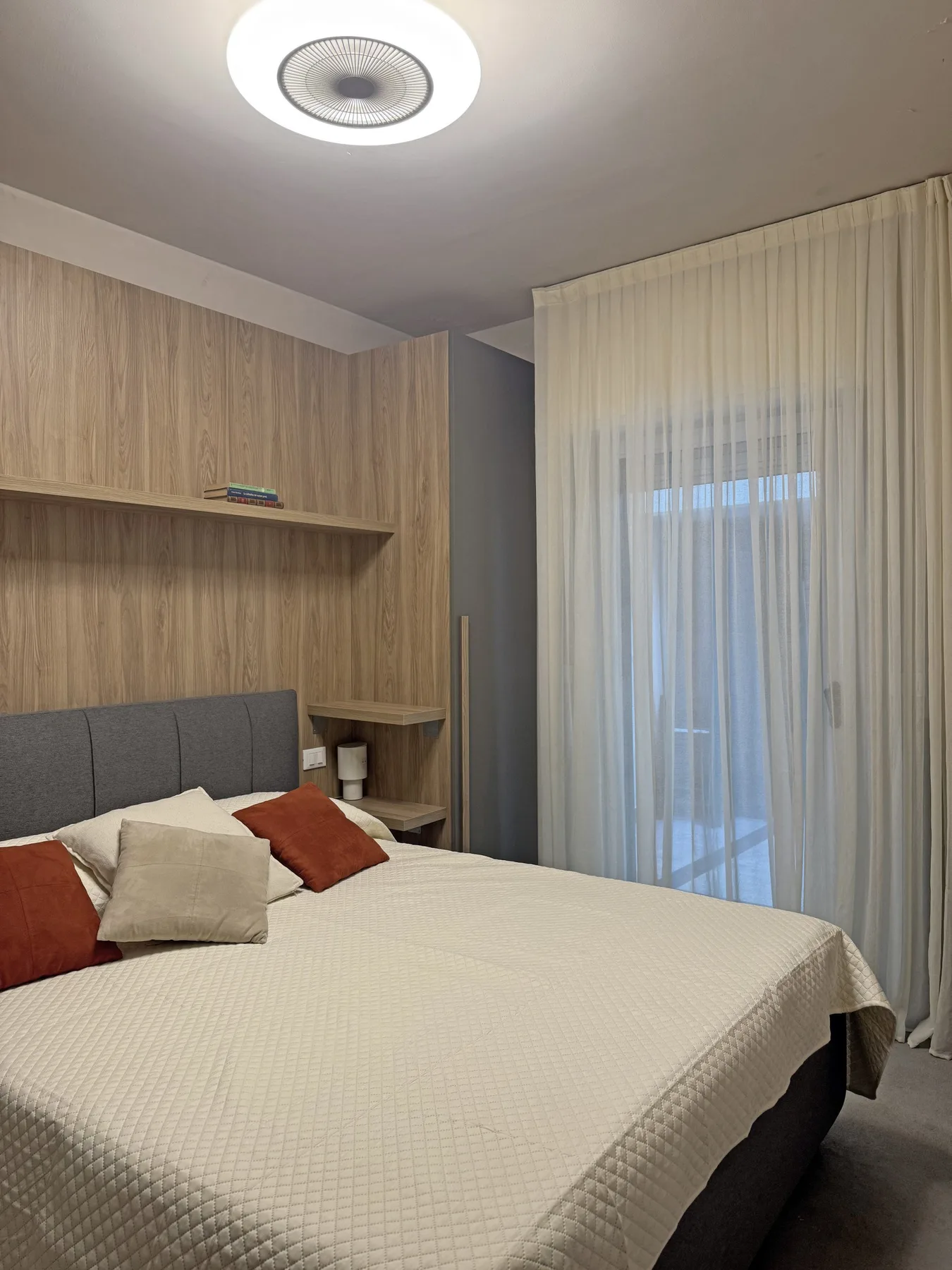 Dormitorio con una cama grande, una pared revestida de madera y cortinas largas.