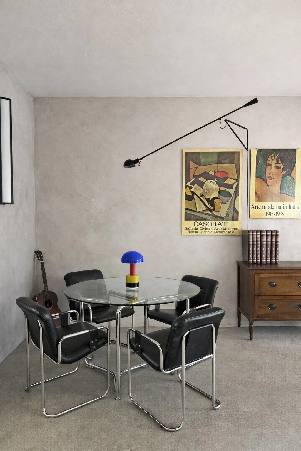 Un comedor con una mesa de vidrio, asientos de metal y carteles enmarcados en la pared.