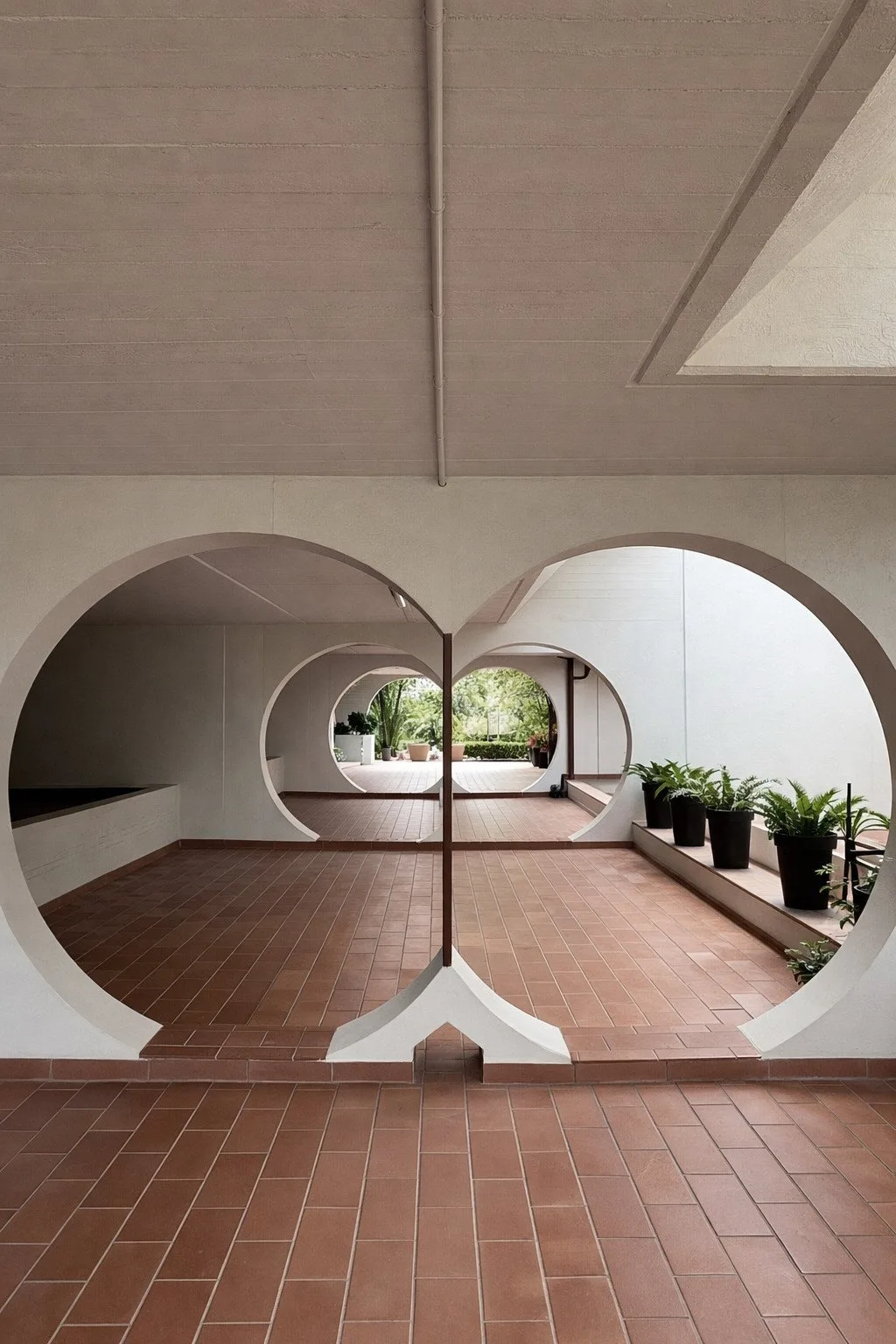 Un patio interior embaldosado enmarcado por grandes aberturas circulares, con plantas en macetas a un lado.