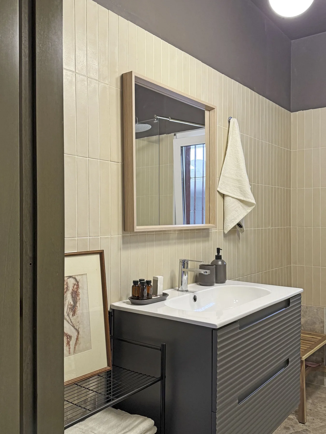 Un lavabo de baño con azulejos, espejo, lavabo y toalla colgada.