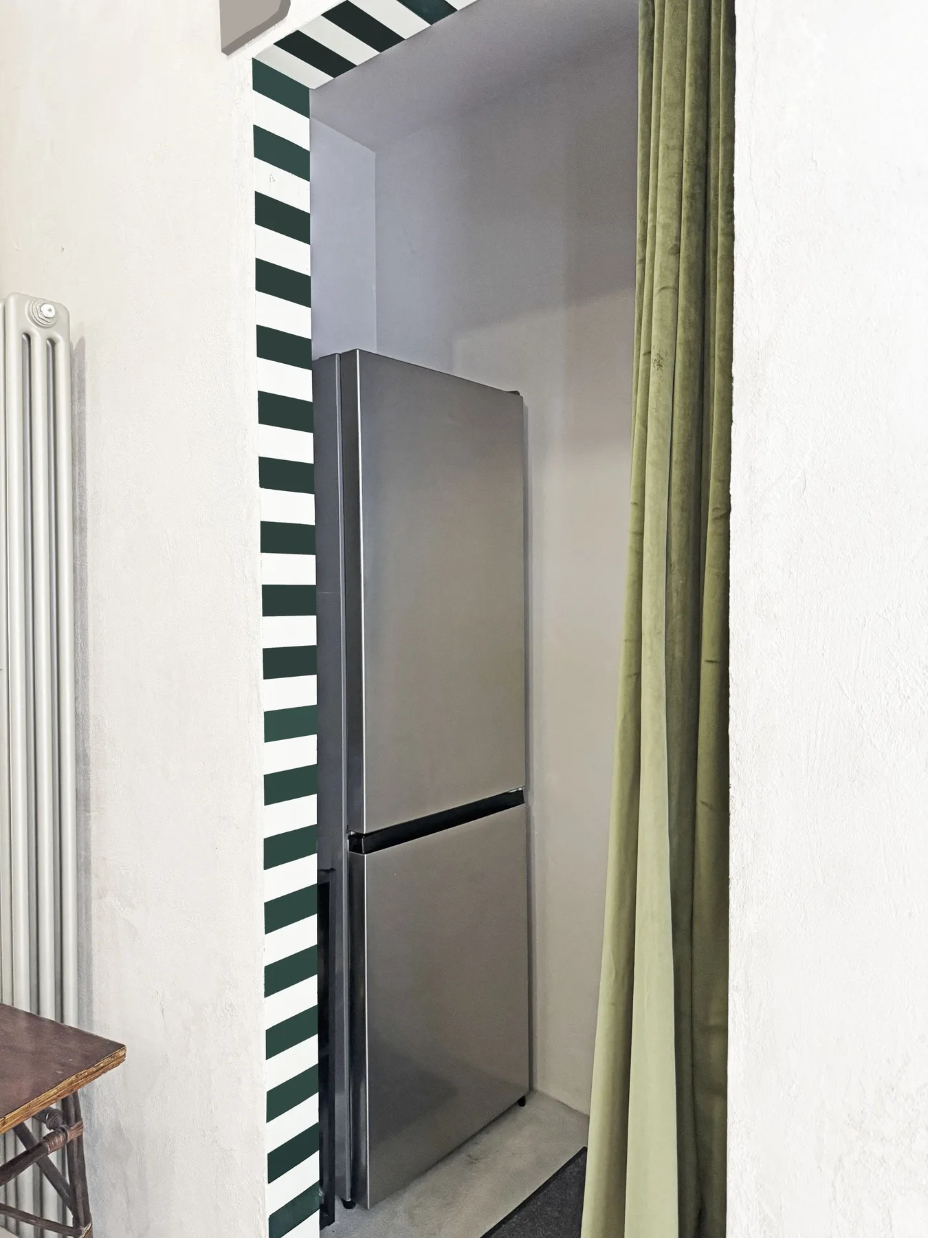Un refrigerador está en un rincón empotrado de cocina junto a una cortina verde.