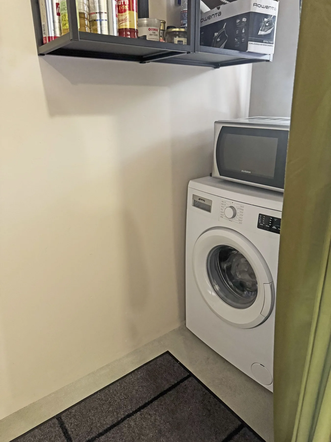 Una zona de lavandería con una lavadora y un estante de productos para el hogar.