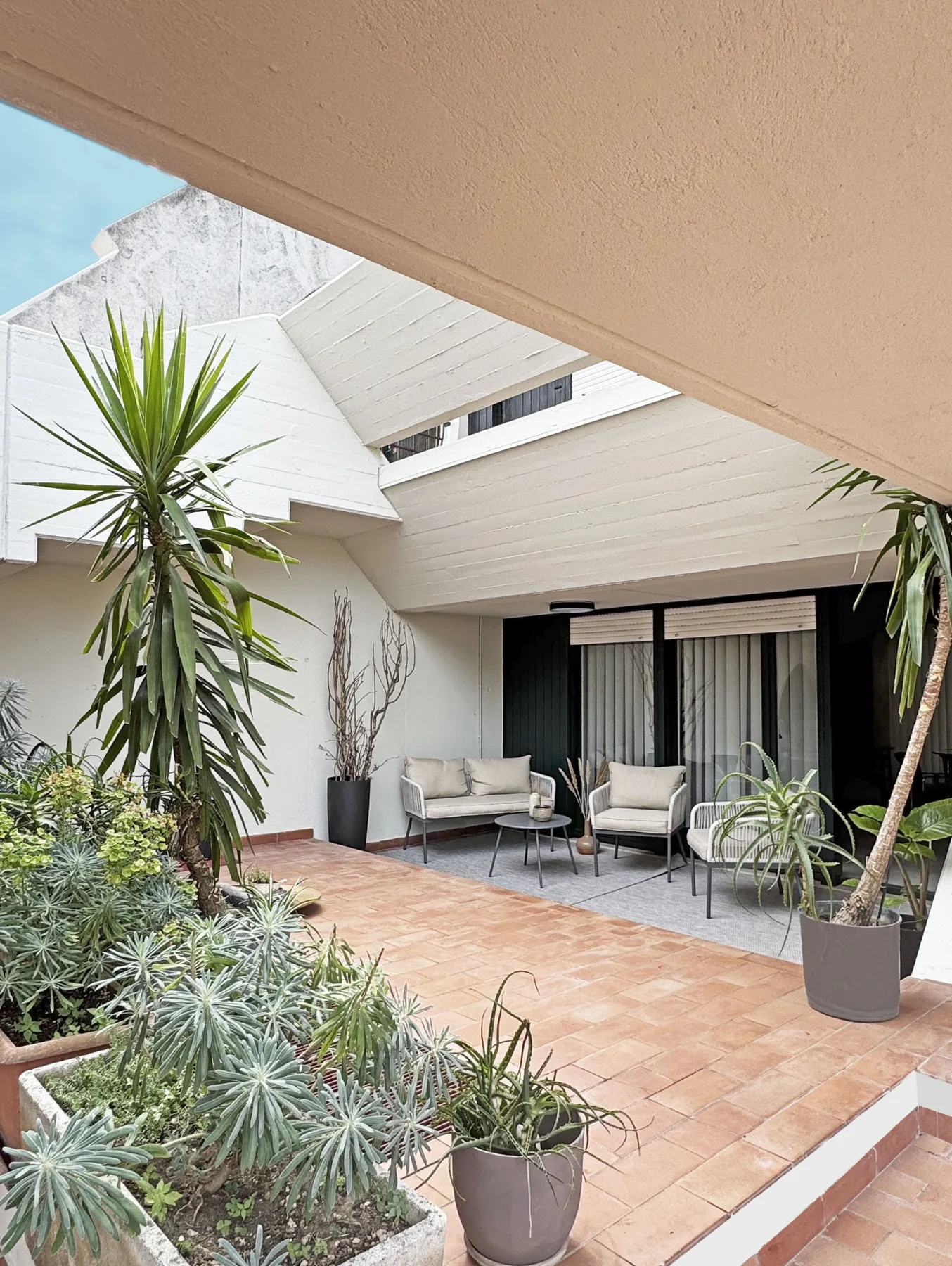 Un patio de baldosas con asientos al aire libre y plantas en macetas junto a la casa.