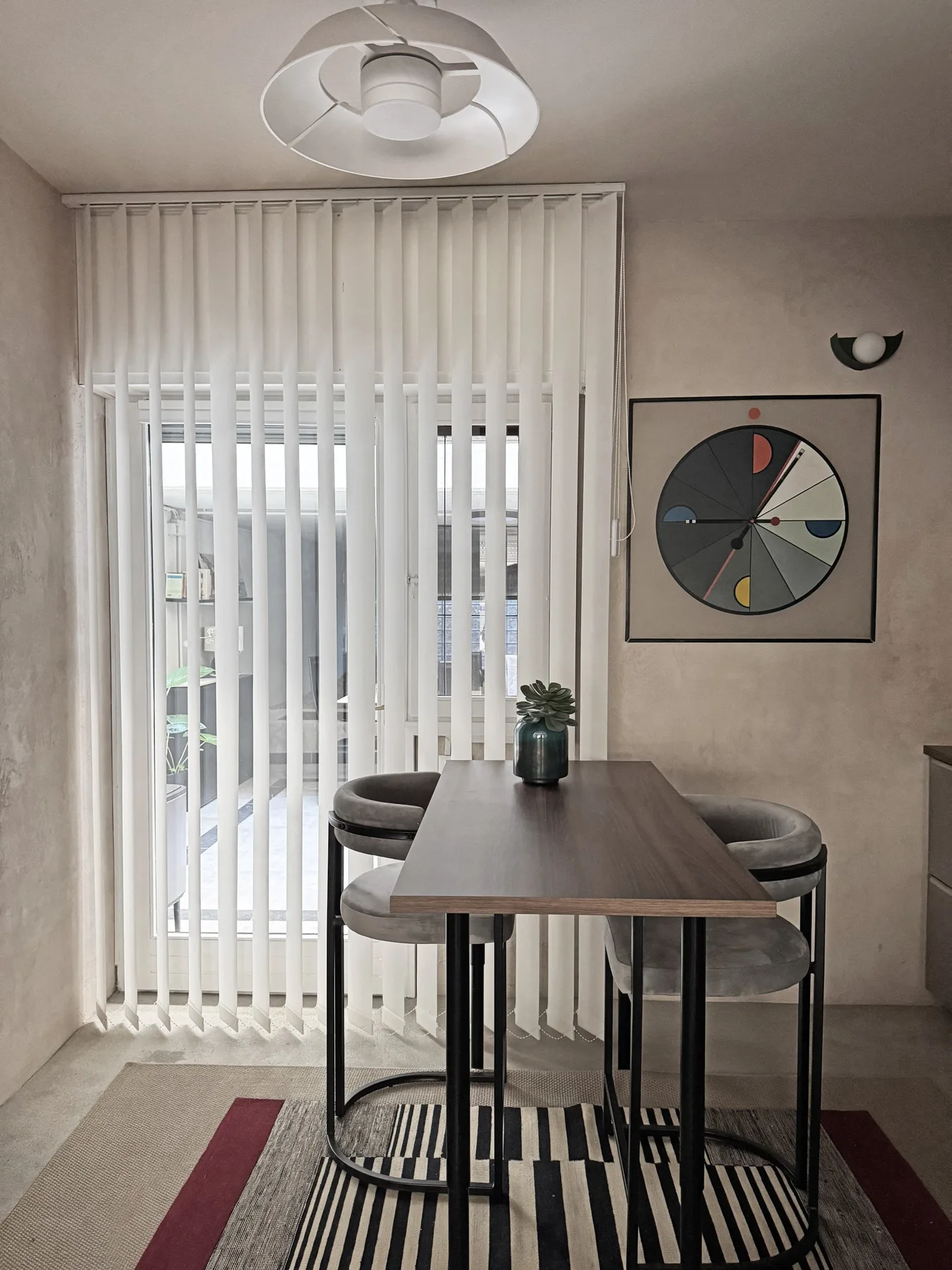 Comedor con mesa, asientos y persianas verticales que cubren una puerta de vidrio.
