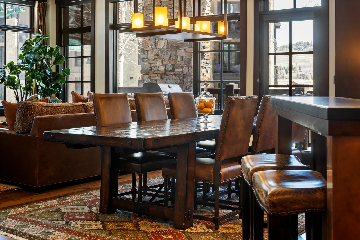 A dining area with a long wooden table, seating, and large windows.