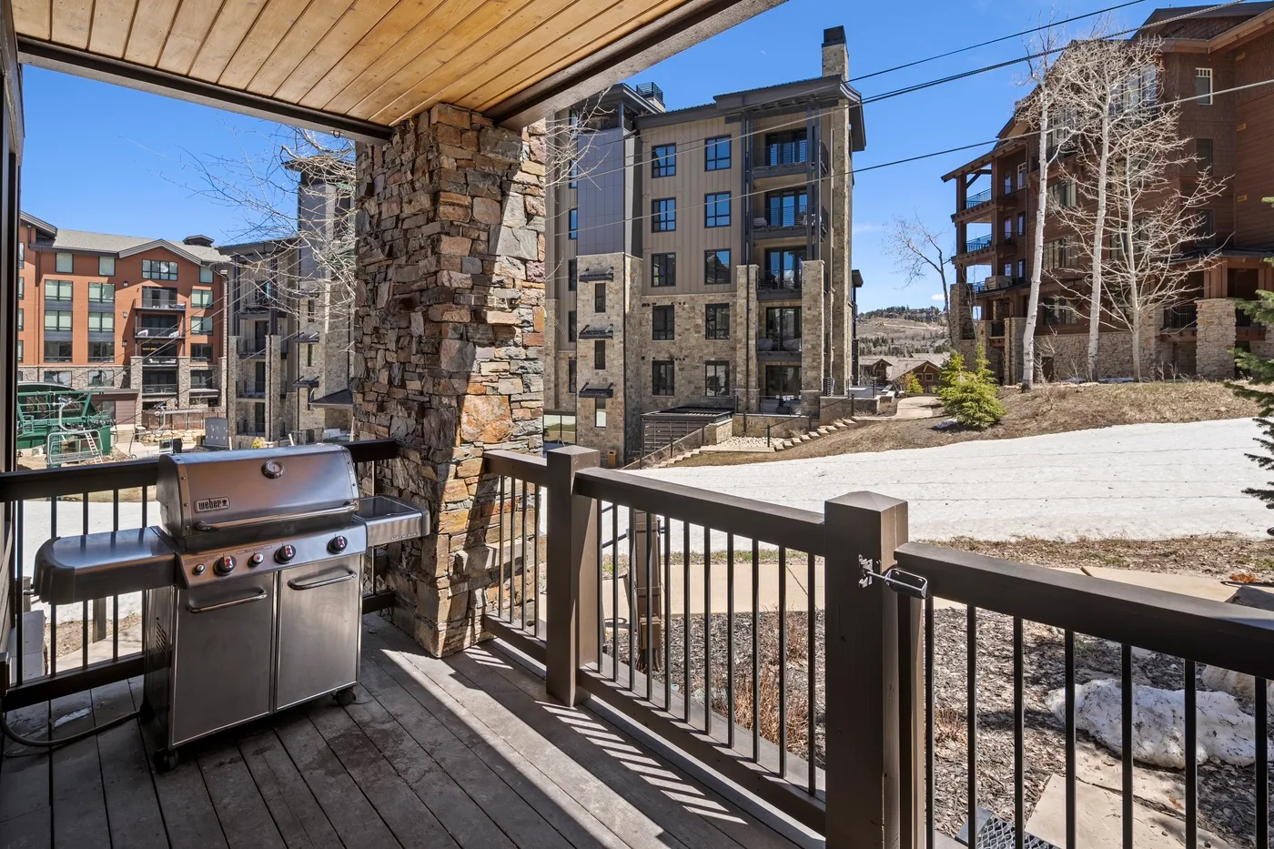 A covered outdoor deck with a grill overlooks several apartment buildings.