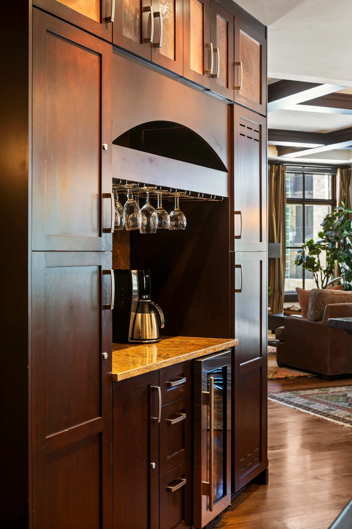 A built-in wooden bar area with hanging glassware opens onto a living room.