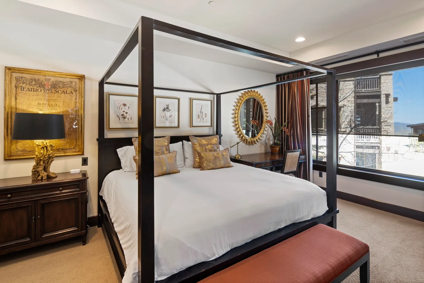 A bedroom with a large four-poster bed and windows overlooking nearby buildings.