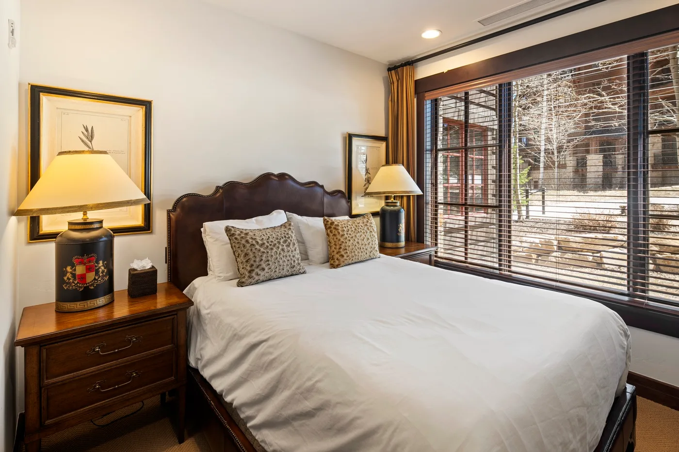 A bedroom with a large bed, bedside tables, and a window with blinds.