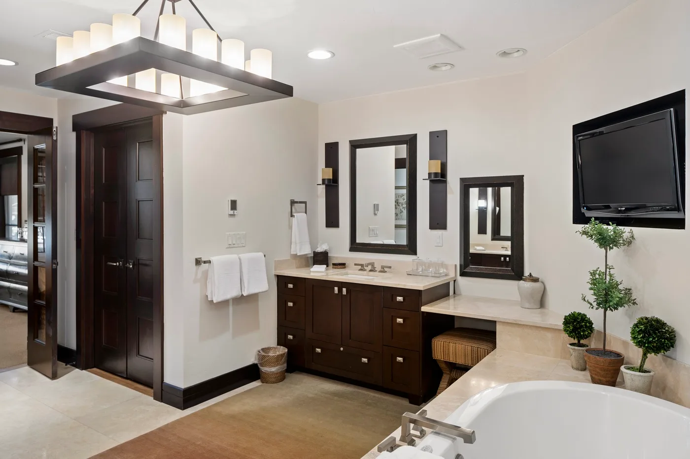 A bathroom with a double vanity, bathtub, and wall-mounted television.