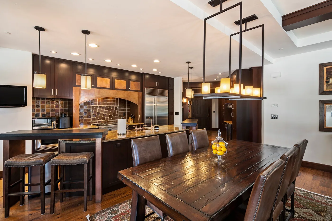 A dining area with a long wooden table beside an open kitchen.
