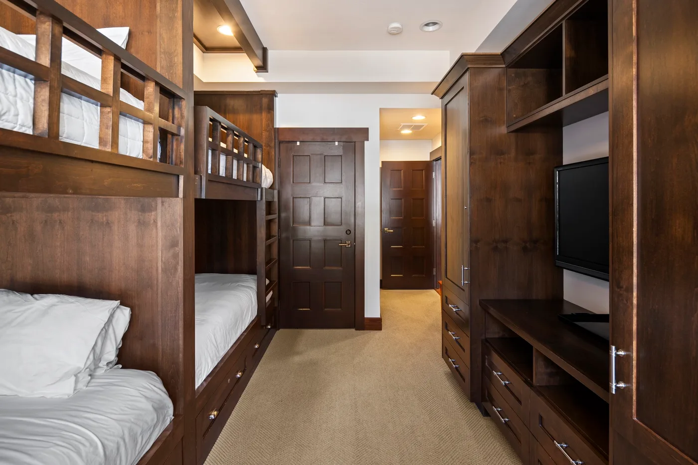 A bedroom with wooden bunk beds and built-in cabinetry along a carpeted passage.