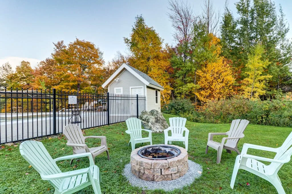 An outdoor seating area surrounds a circular stone fire pit beside a black metal fence.