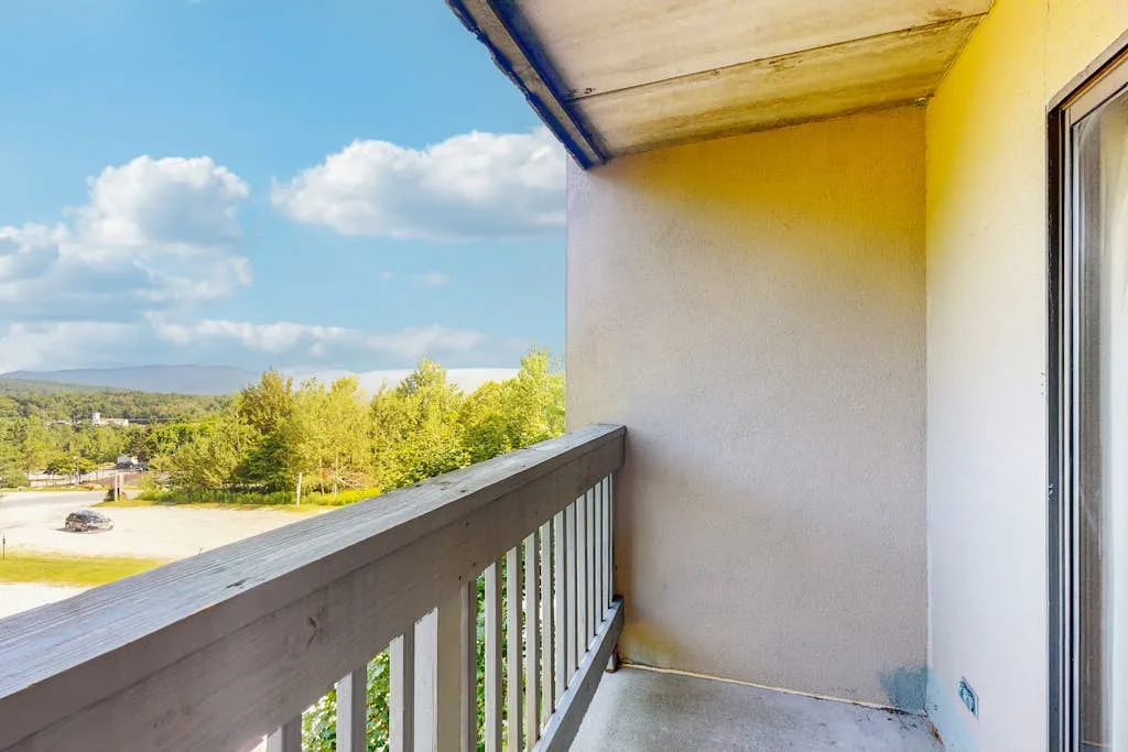 A balcony overlooks trees and distant hills beneath a partly cloudy sky.