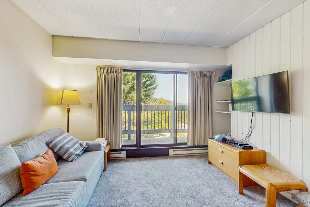 A living room with seating, a television, and glass doors opening onto a balcony.