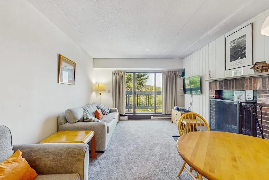 A living room with seating, a television, and a sliding glass door opening to a balcony.