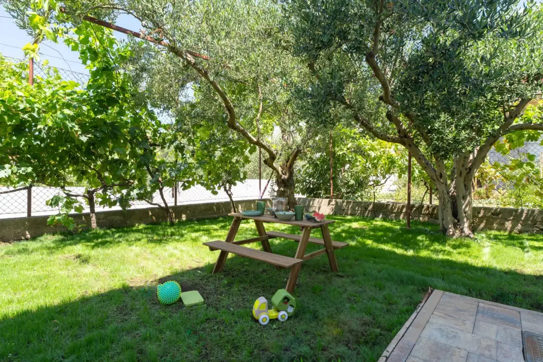 Una zona de césped con un espacio infantil con juguetes, un columpio y una zona de asientos para niños.