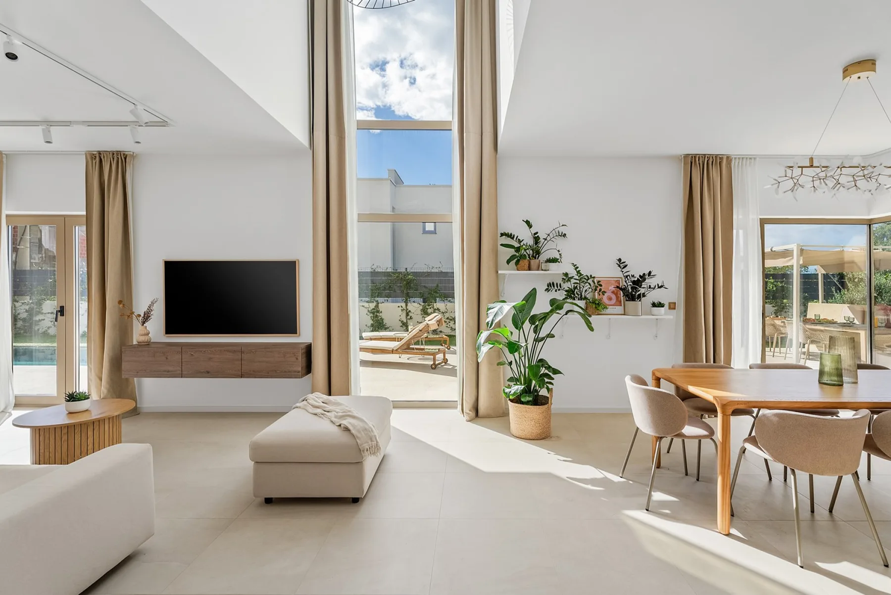 La amplia zona de estar cuenta con un cómodo sofá, un televisor de pantalla plana con sonido envolvente y una pared acristalada con vistas a la zona de la piscina