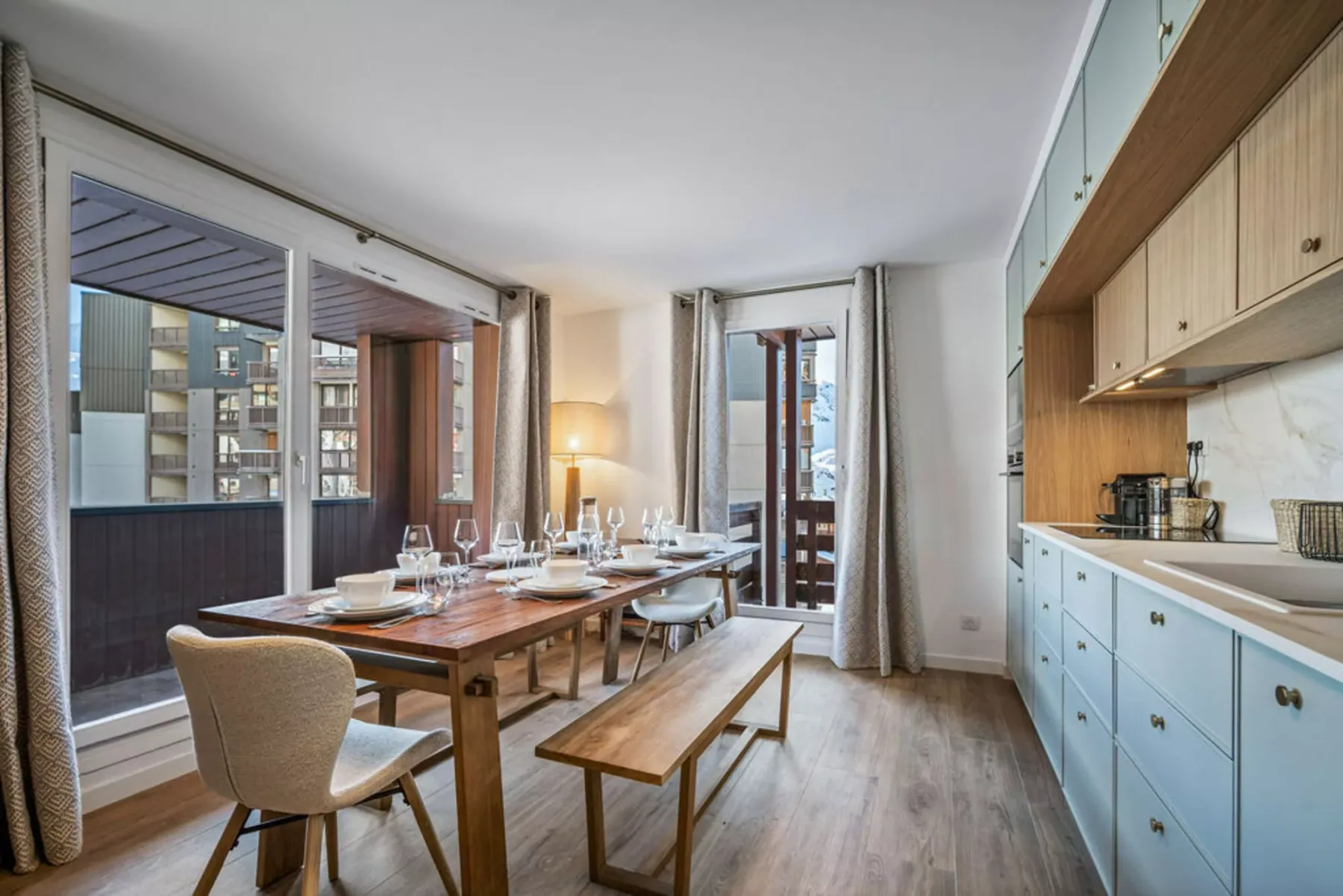 A dining area with a long wooden table beside a compact kitchen.