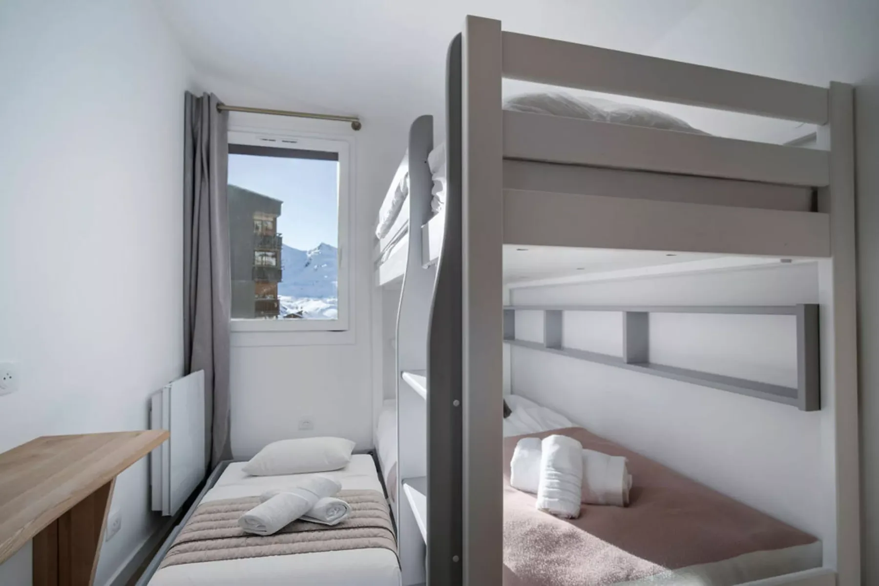 A compact bedroom with bunk beds, single beds, and a window overlooking snowy mountains.