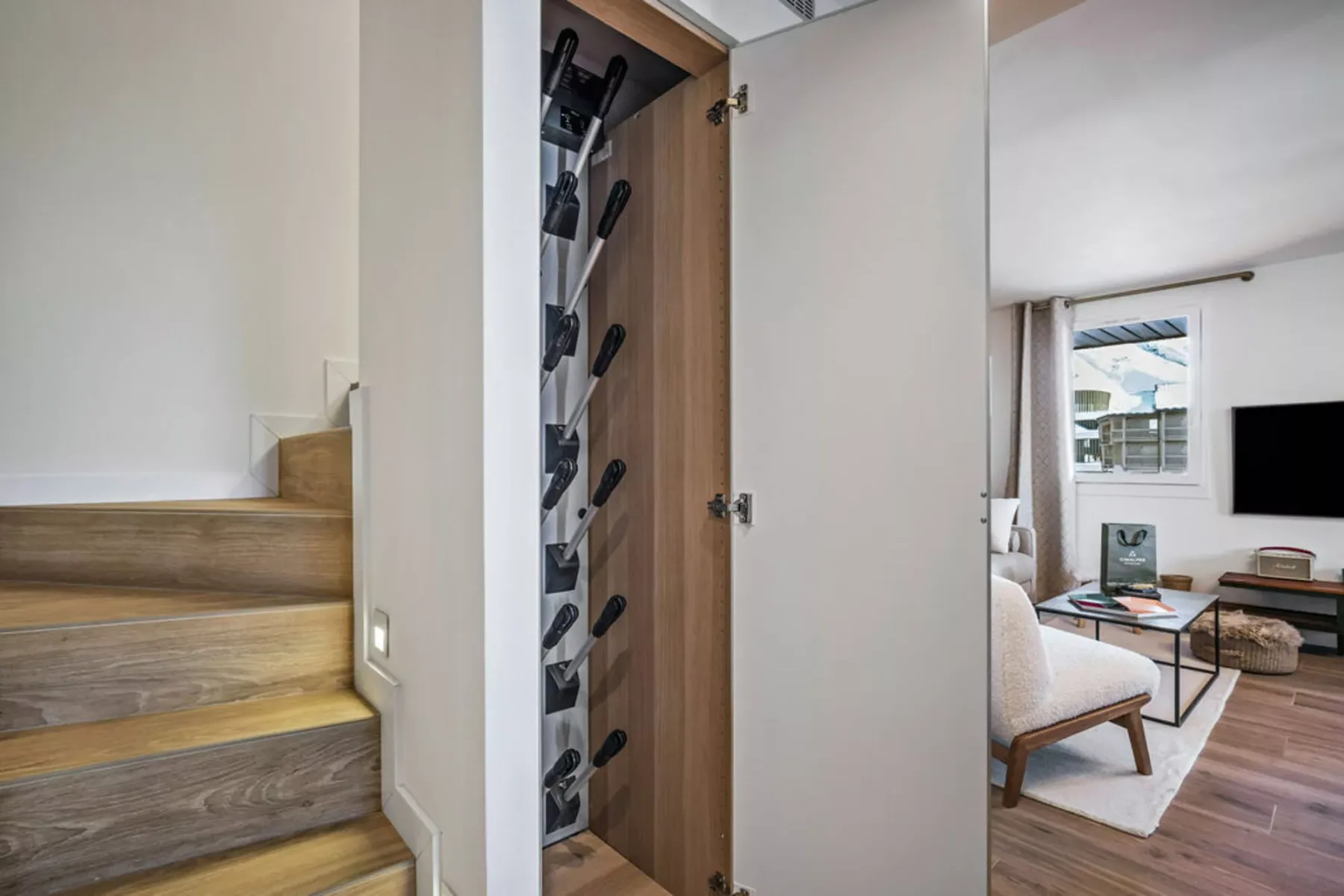 A stairway beside an open storage cabinet, with a seating area visible beyond.
