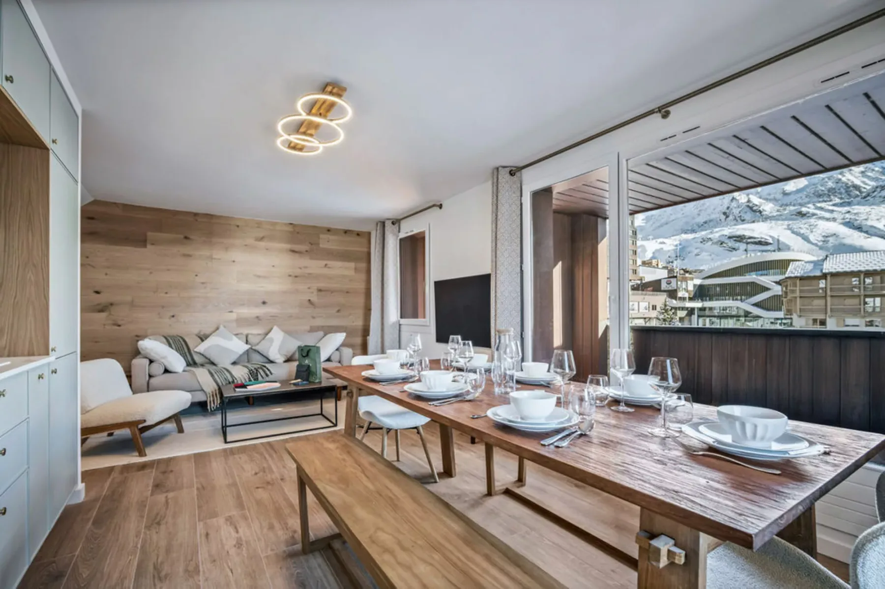A dining area with a set table beside large windows overlooking snowy mountains.