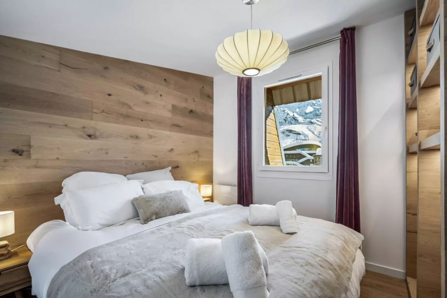 A bedroom with a bed, wood-paneled wall, and window overlooking snowy scenery.