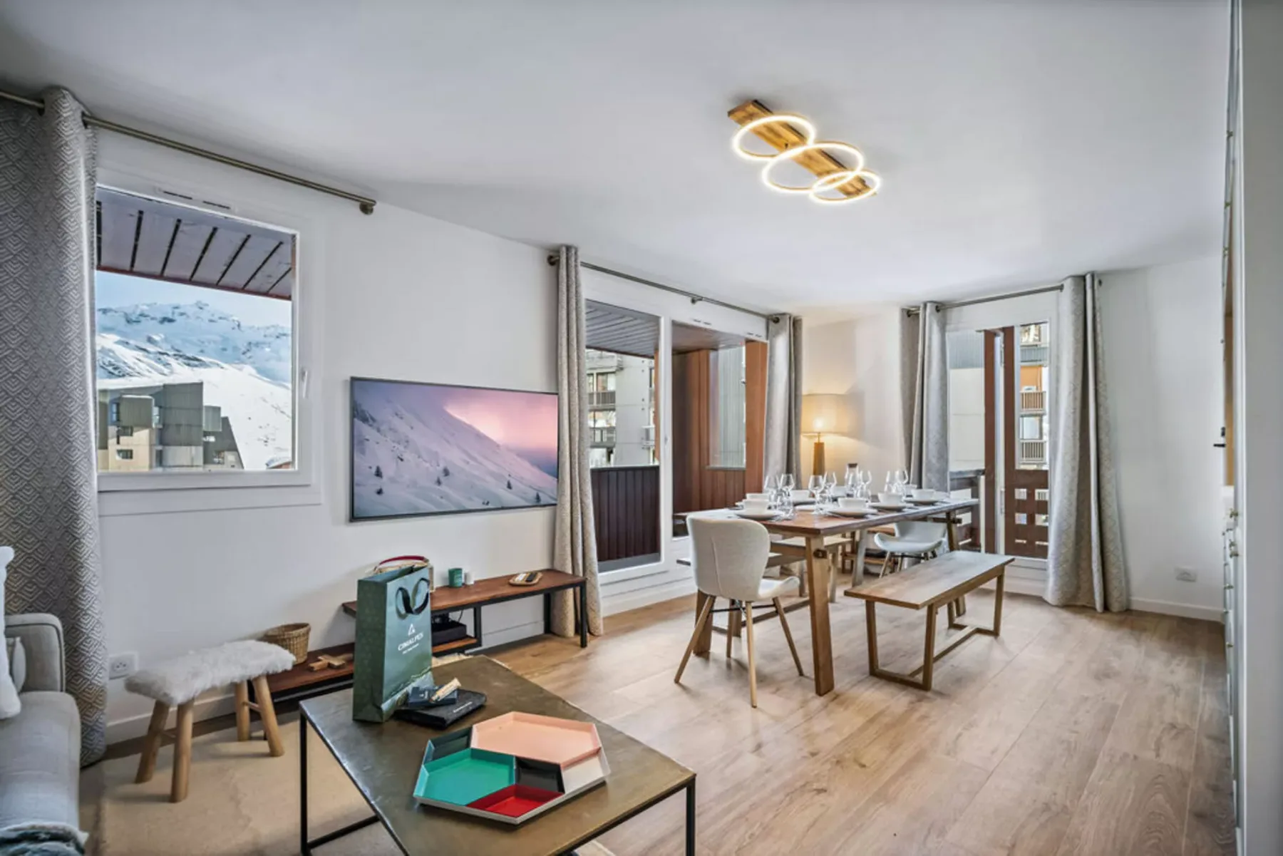A bright dining and living area with a wooden table and large windows.
