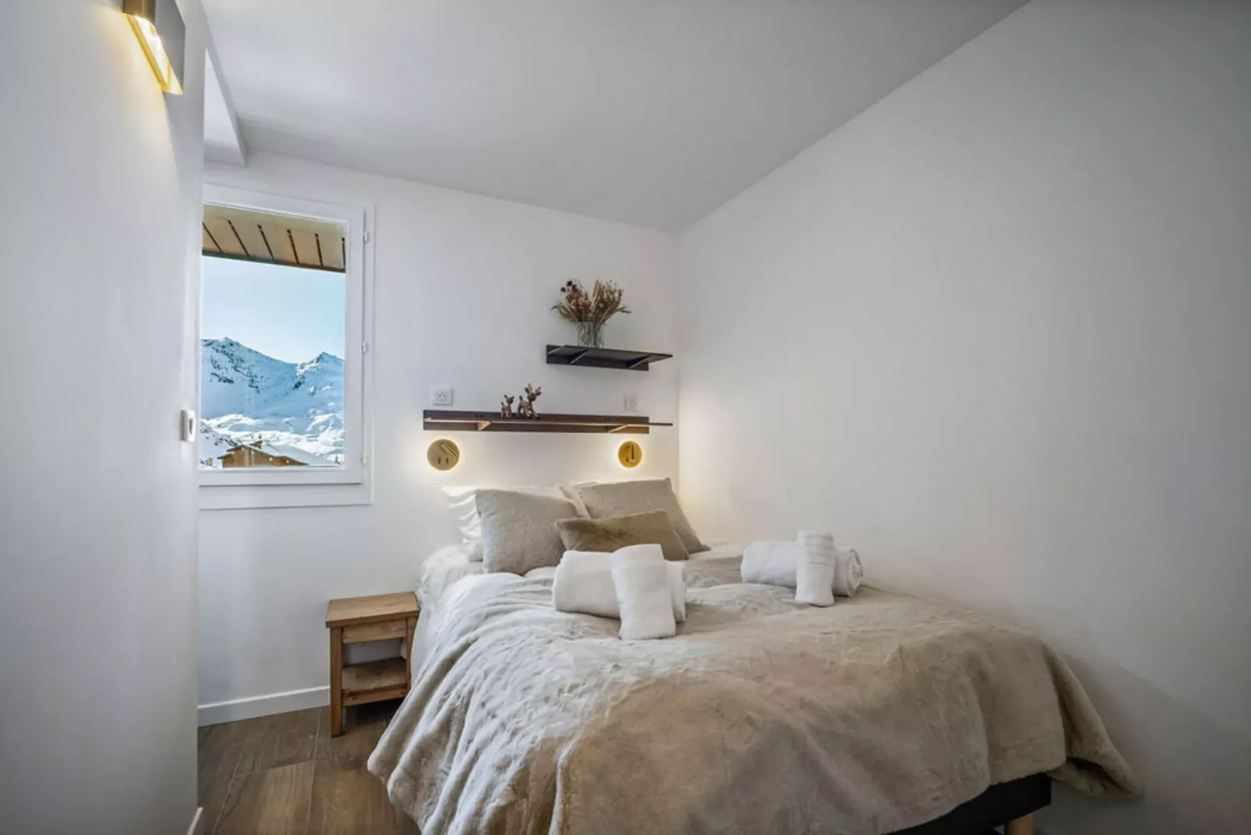 A bedroom with a bed, neutral bedding, and a window overlooking snowy mountains.