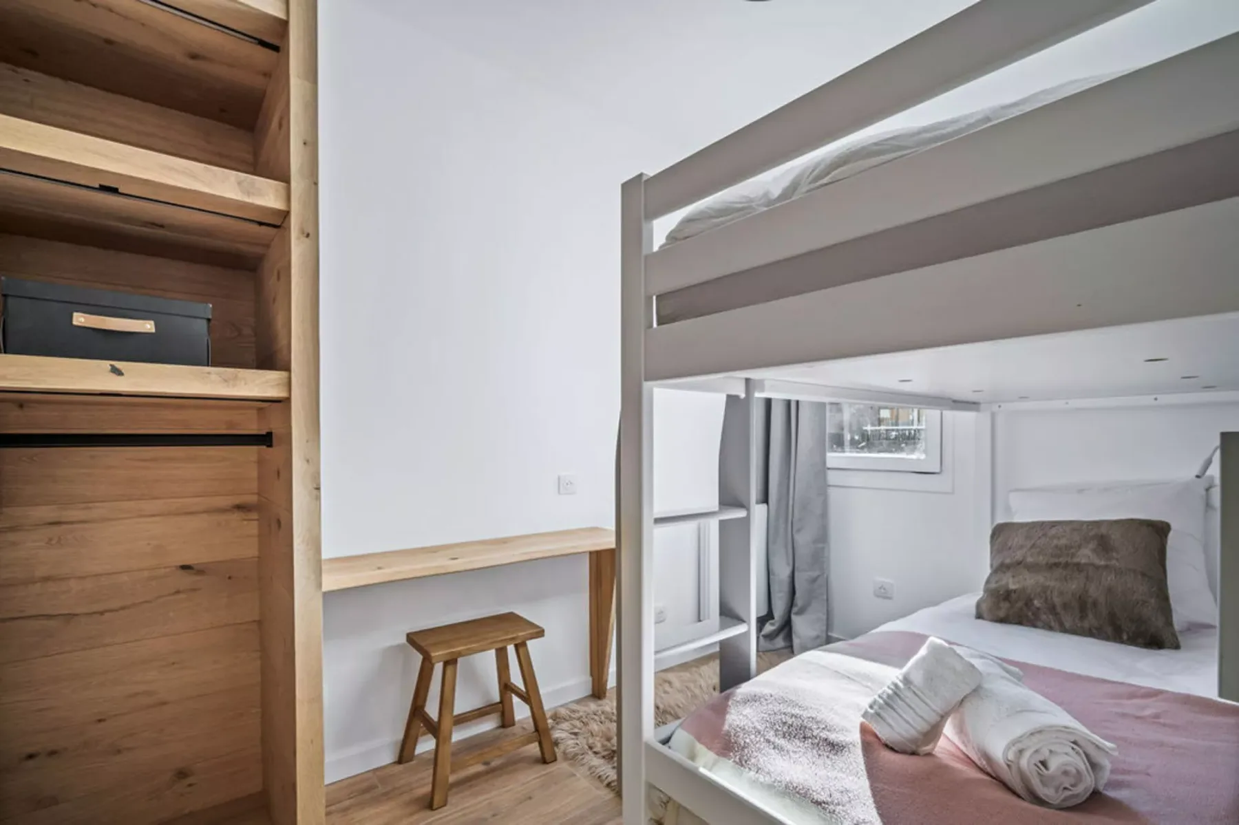 A compact bedroom with a bunk bed, wooden shelving, and a small stool.