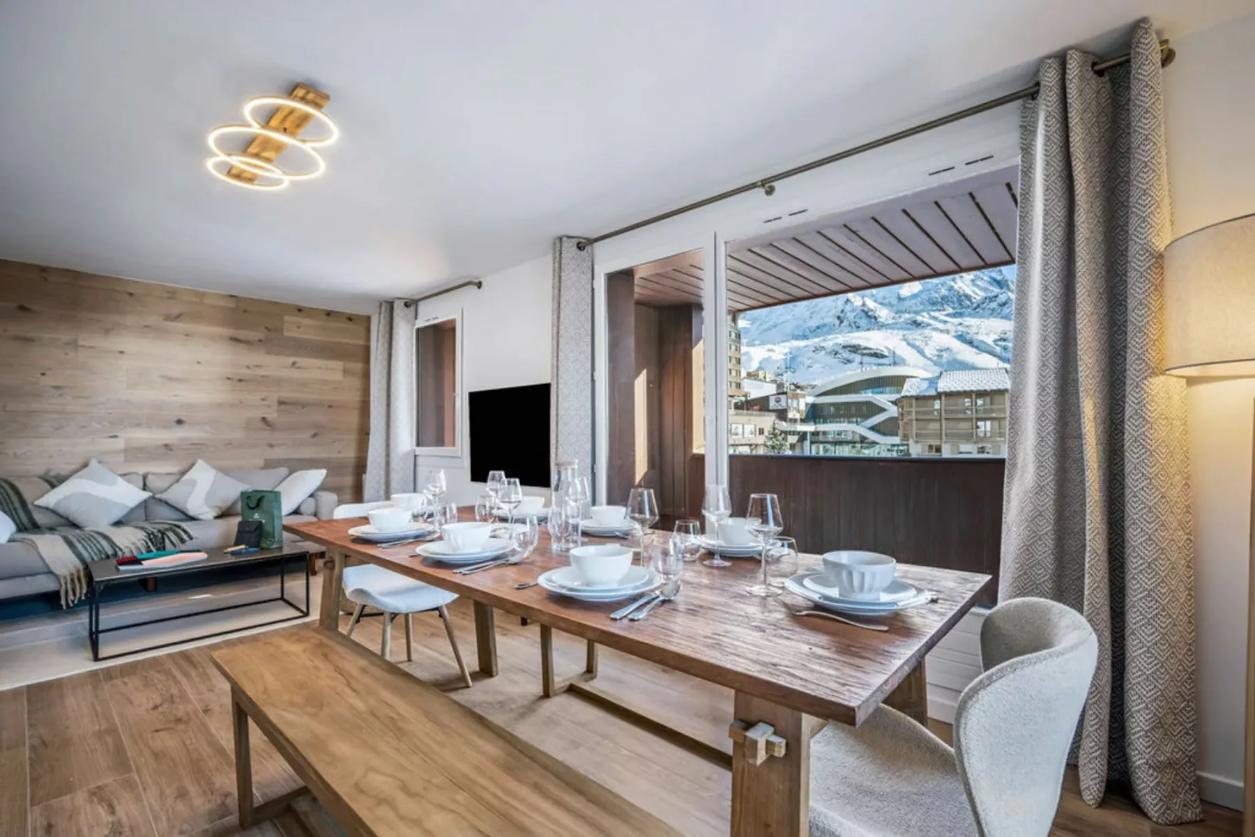 A dining area with a set table beside large windows overlooking snowy mountains.