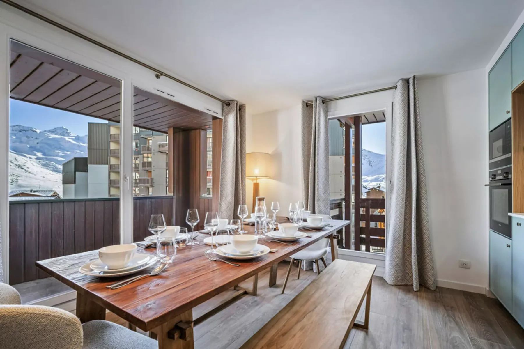 A dining area with a long wooden table set beside large windows overlooking snowy mountains.