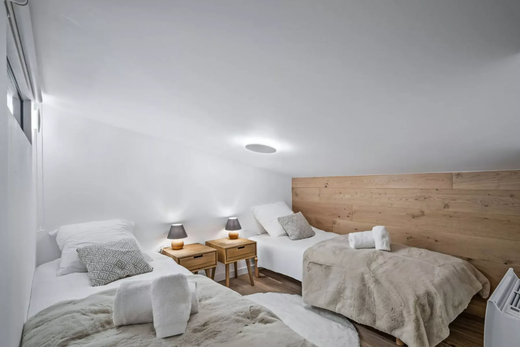 A bright bedroom with two beds and a wood-paneled wall.