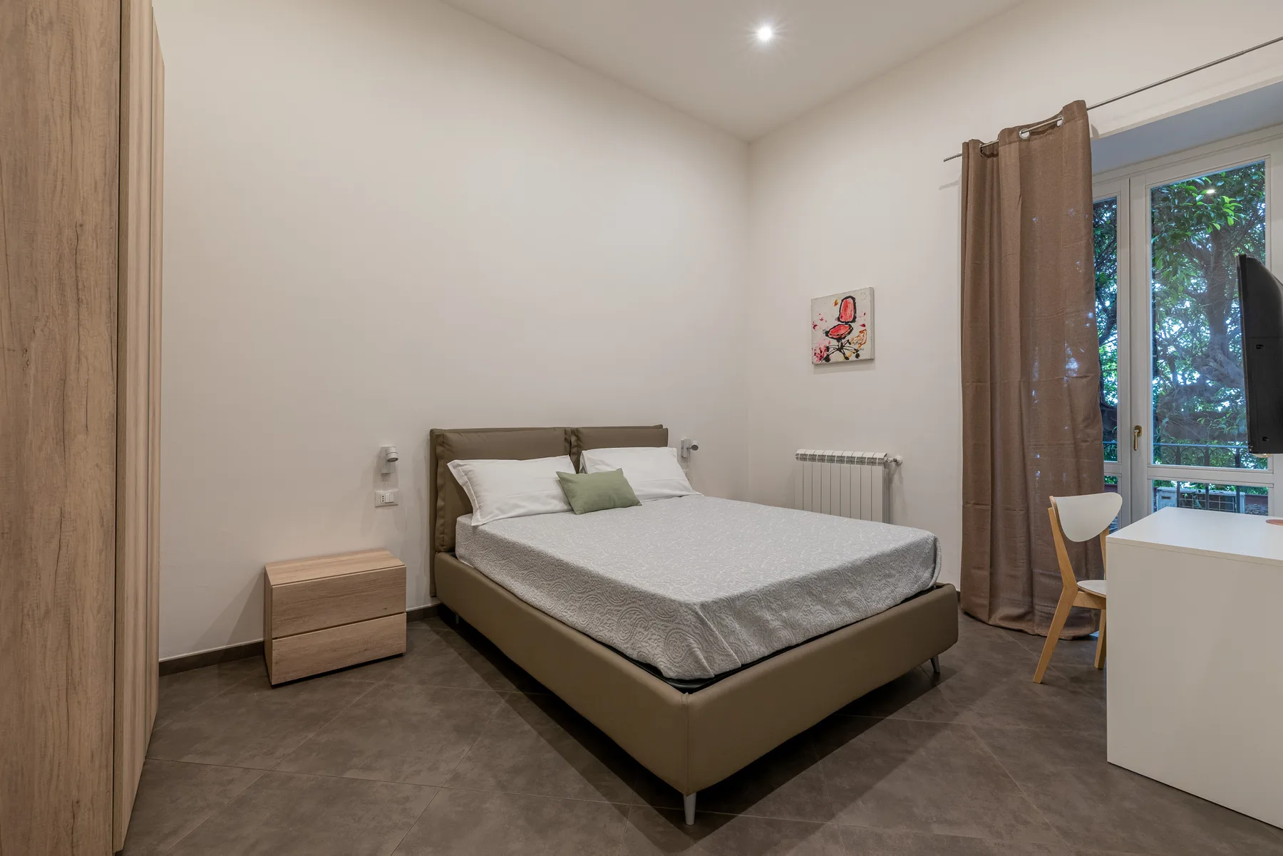 A bedroom with a bed beside a curtained window.