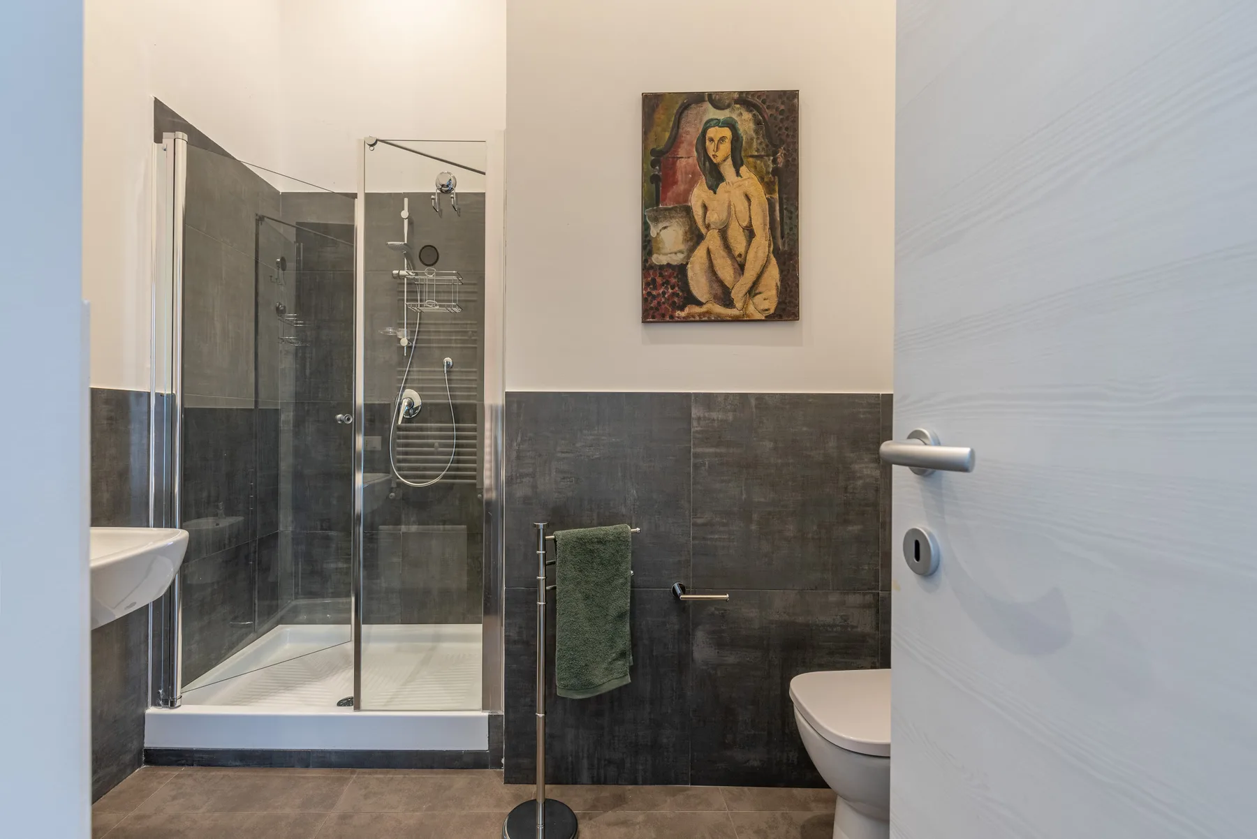 A bathroom with a glass shower, wall-mounted artwork, and a partially visible toilet.