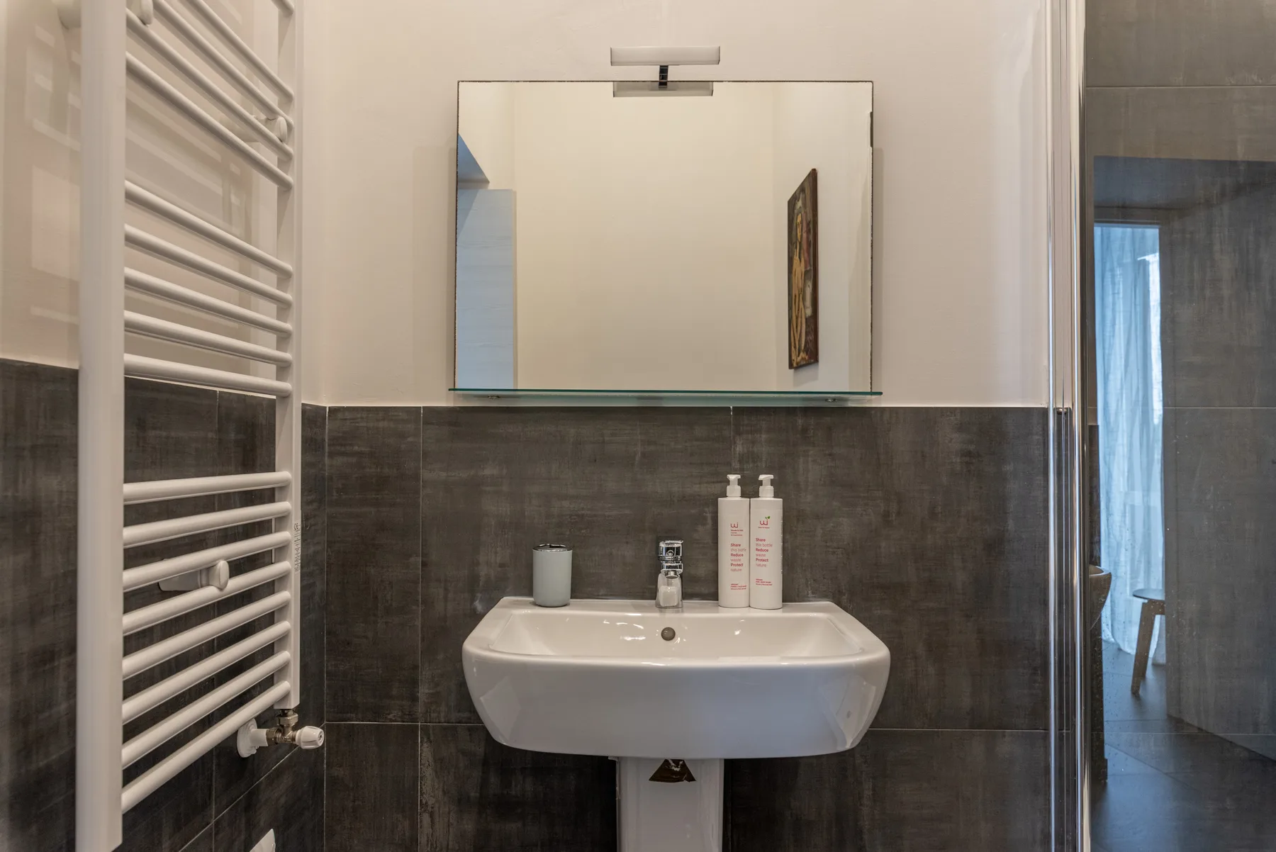 A bathroom sink beneath a wall mirror, with dark tile along the lower walls.