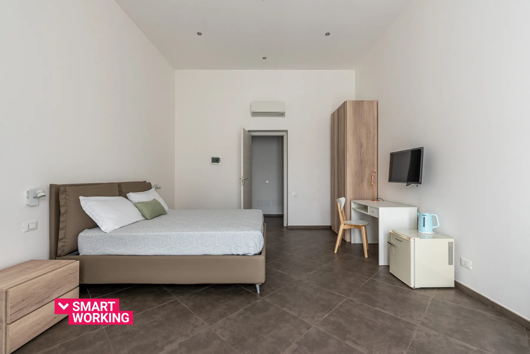 A modern bedroom with a double bed, a desk, and a wall-mounted television.