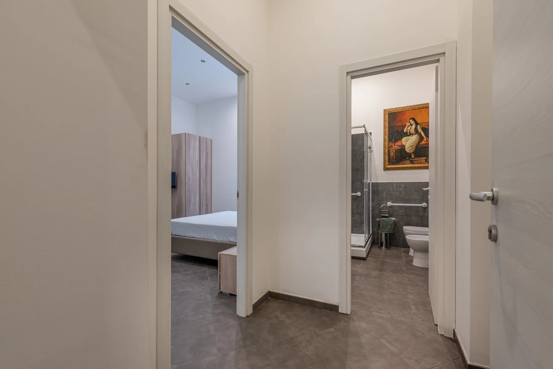 A hallway connects a bedroom and bathroom, with a framed picture on the bathroom wall.