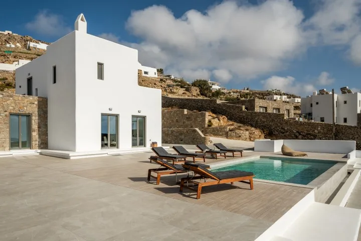 A modern white villa opens onto a terrace with a swimming pool and loungers.