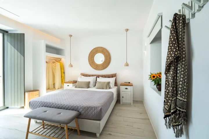 A bright bedroom with a bed, bedside tables, and a round wall mirror.