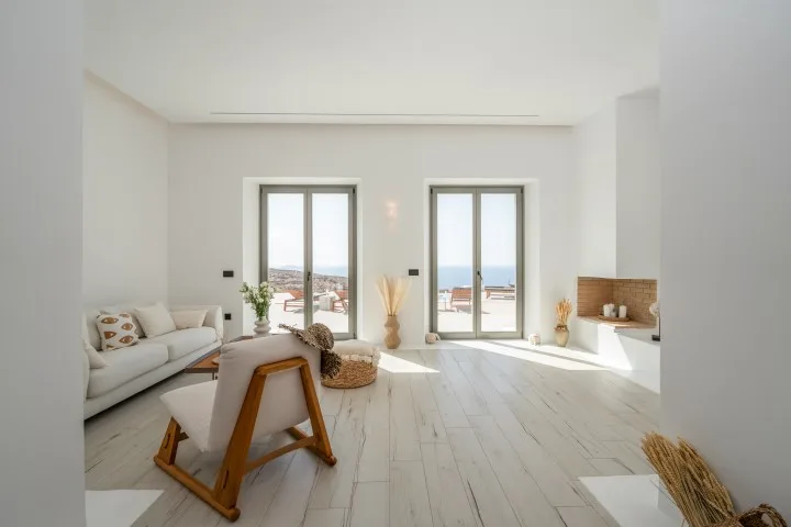 Bright living room with seating beside tall glass doors overlooking the sea.