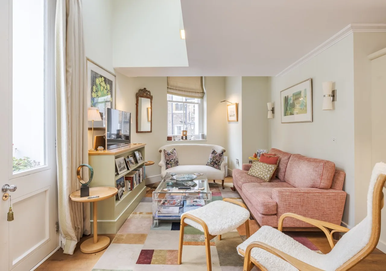 A bright living room with pink seating, a glass coffee table, and large windows.