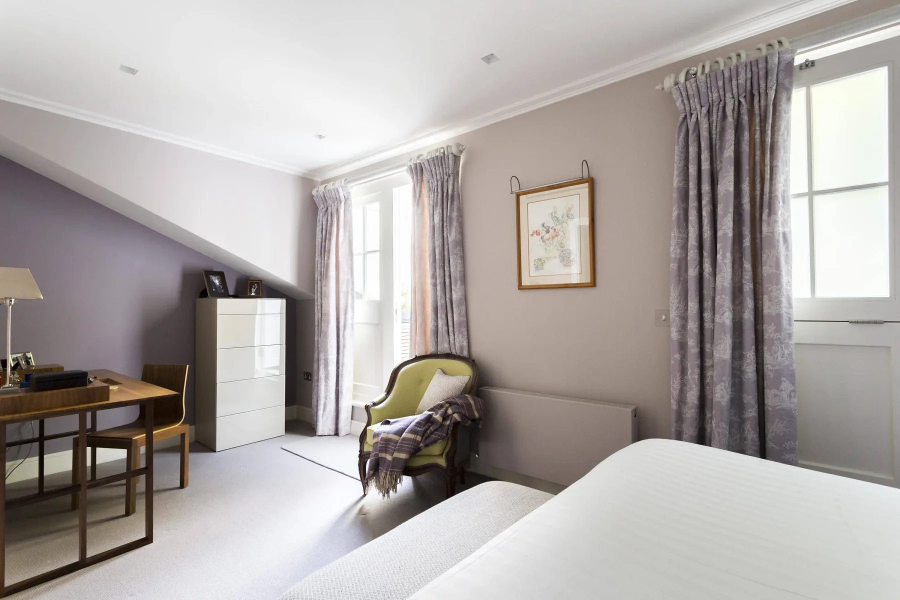 A bright bedroom with a bed, desk, and curtained windows.